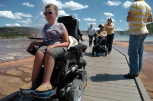 photo of two wheelchair users on wooden pathway with hot springs on their sides