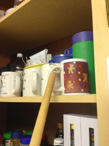 wooden dowel with a hook on the end grabbing a coffee cup out of a cupboard