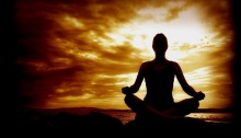picture of a woman sitting cross-legged in a meditation pose with the sun setting