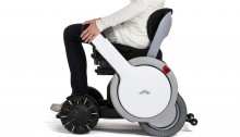picture of the WHILL - a white futuristic and modern looking wheelshir with a woman pushing down the arm