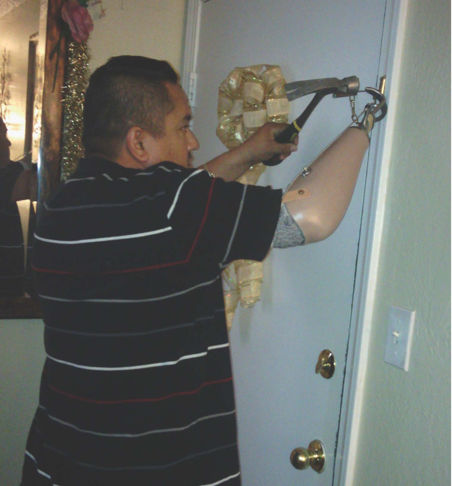 Roslind ( man with arm prosthesis) is fixing a door lock using his hook and an hammer.