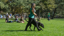 picture of a woman walking with a black service animal on a college campus
