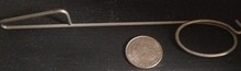 picture of the metal device next to a quarter it is thin and metal and about the length of 5 quarters