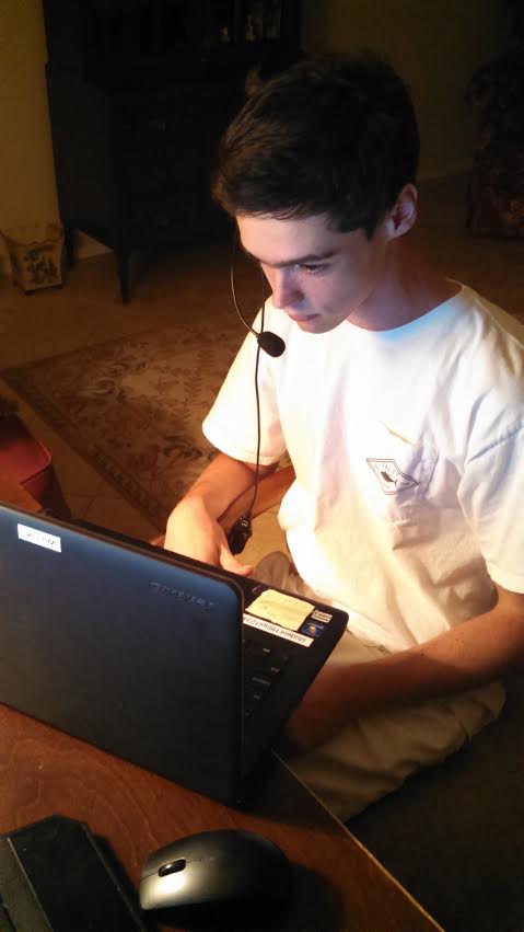 picture of a young causcasian man with brown hari sitting at a desk with a headset and laptop on