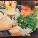 Picture of a little boy sitting at a desk using a communicaiton tablet