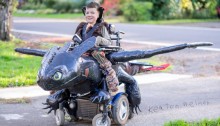 picture of young boy and his wheelchair is an elaborate flying froglike creature he is smiling