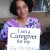 picture of a smiling woman seated and holding a placard that says I am a caregiver for my mom