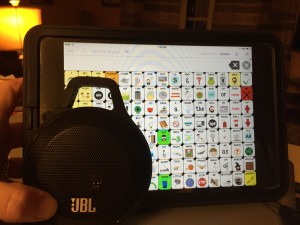 JBL Clip Bluetooth speaker looks like black cirlce small and 2/3rd of the size of the iPad next to the Speak for Yourself app on an iPad mini.