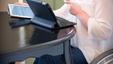 picture of woman using two tablets and smart phone and wheelchair at table