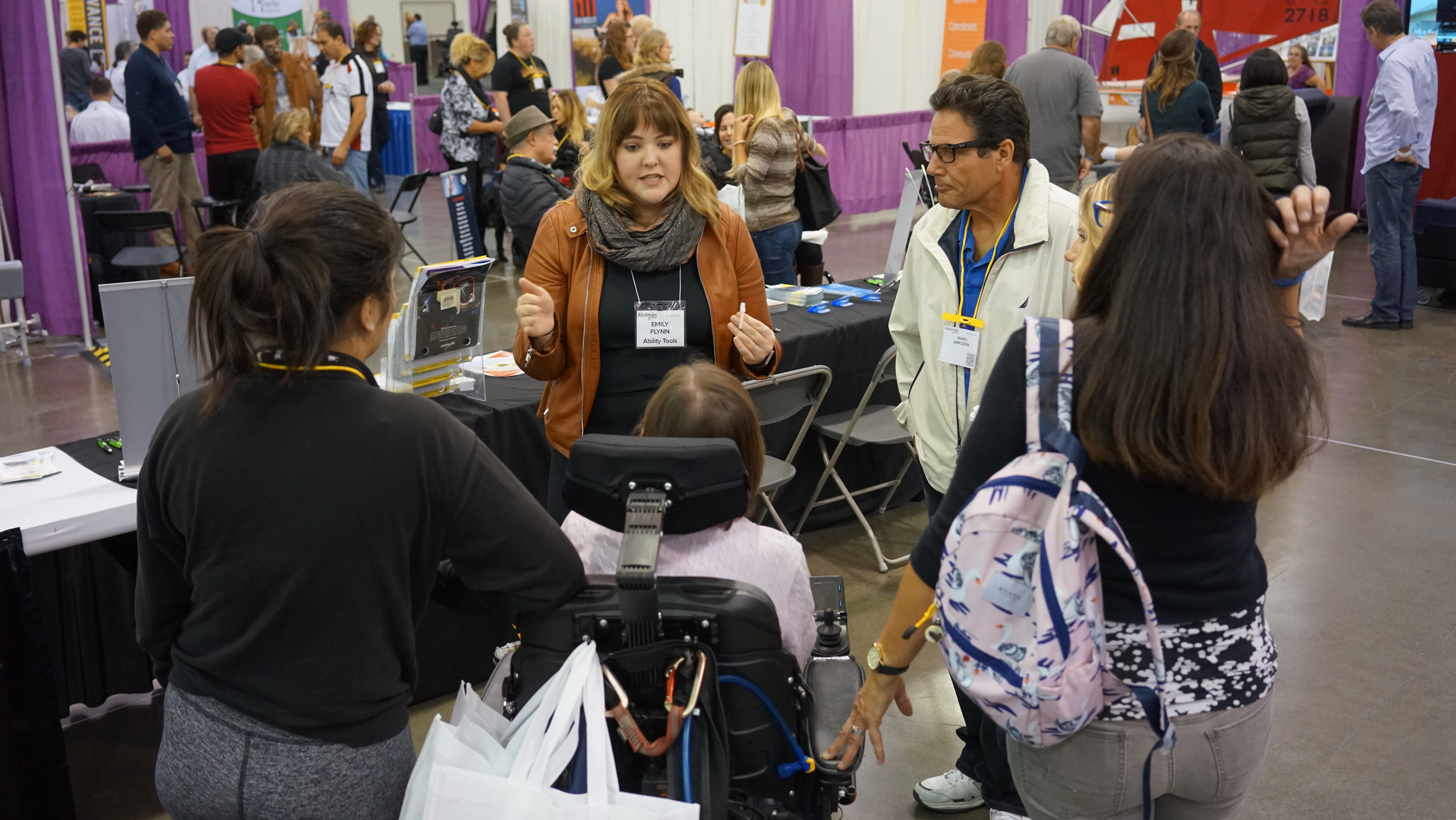 A woman is surrounded by 5 people at a disability resource fair. 