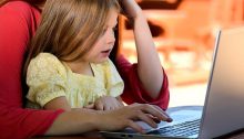 A young girl sits on her mom's lap looking at a laptop together.