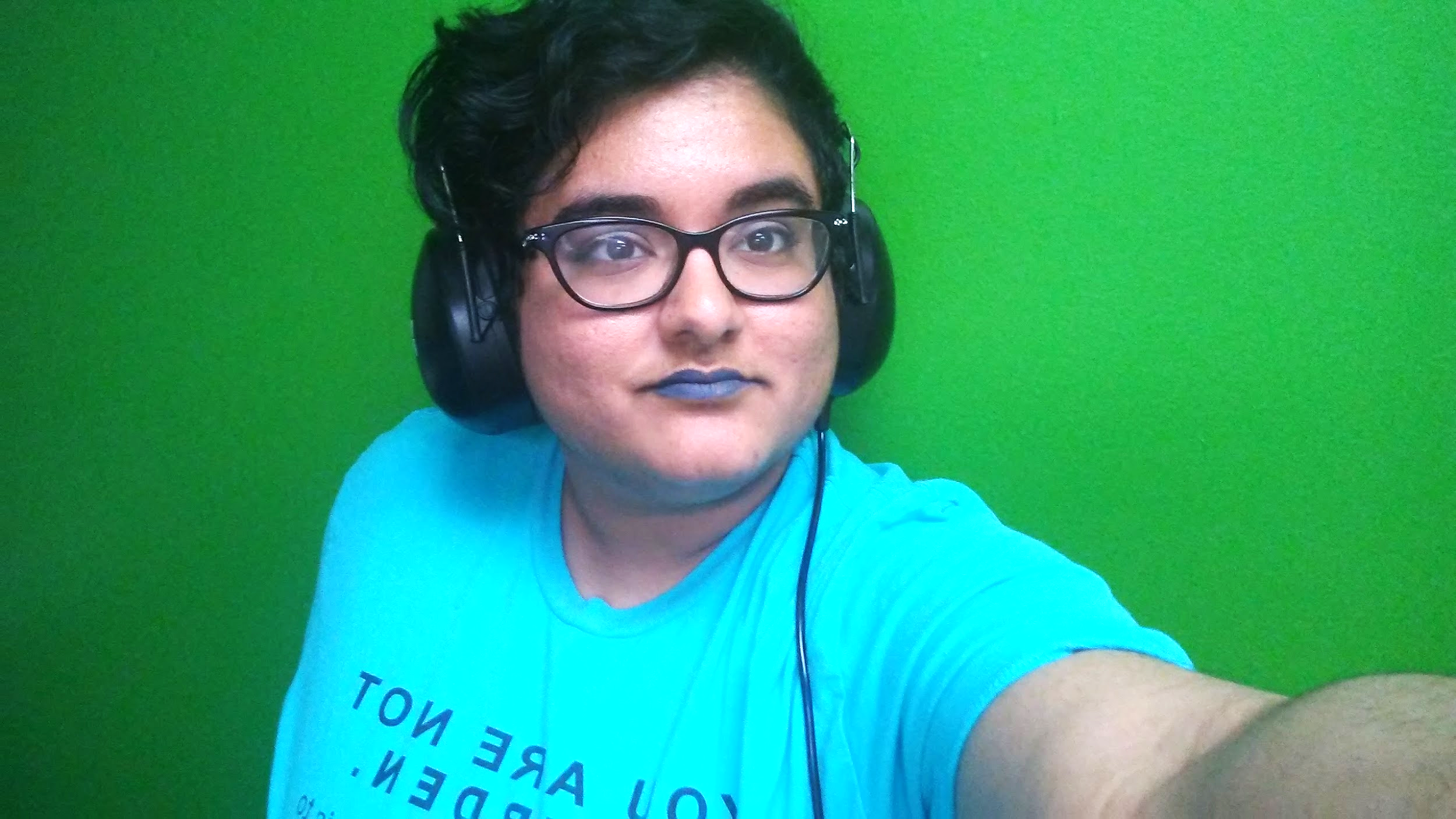 Image is Noor, a tan autistic person with blue lipstick, wearing big headphones