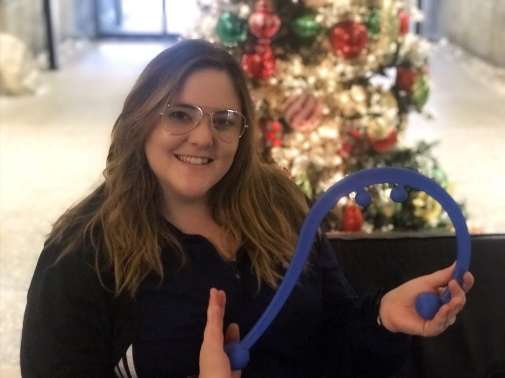 Photo of Emily wearing eyeglasses, holding a blue question-mark shaped apparatus.