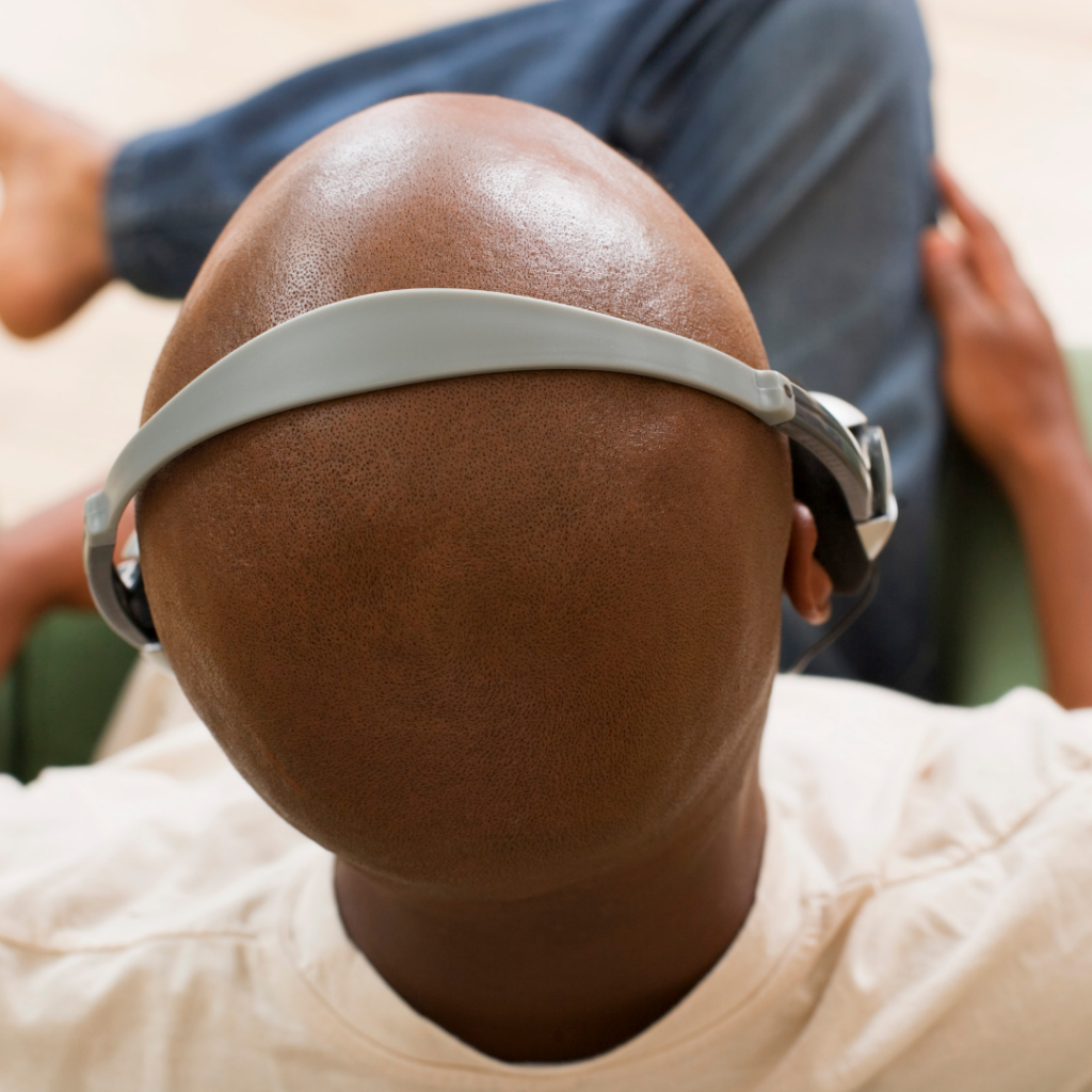 Black male seated facing away from camera, wearing headphones. Legs crossed.