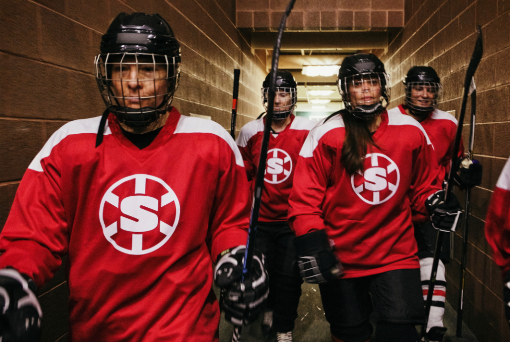 A team of geared up female hockey players walk in a hallway.