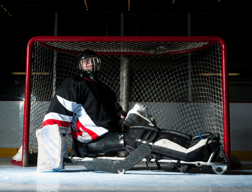 A sled Hockey goalie blocks a shot in front of the net.