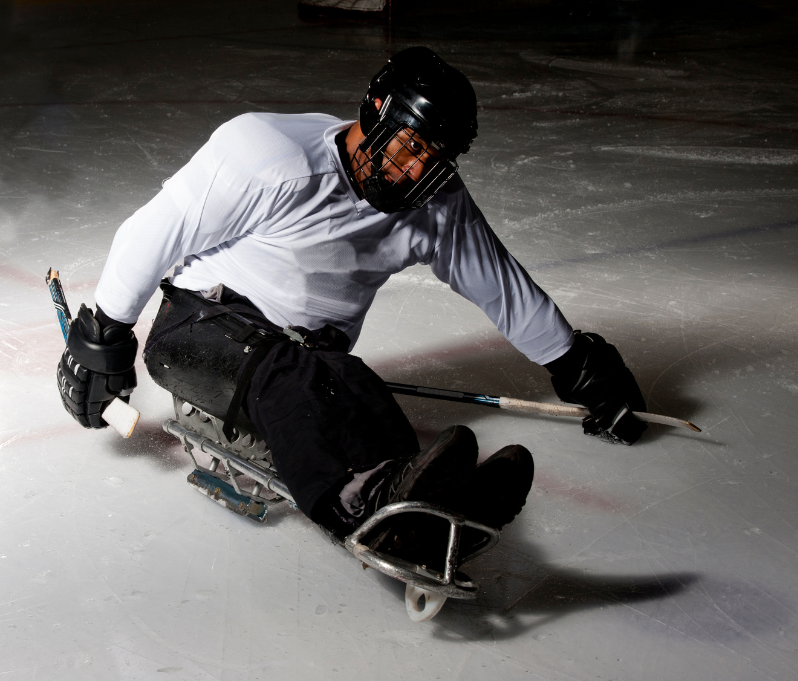 A sled Hockey player pushes forward on the ice.