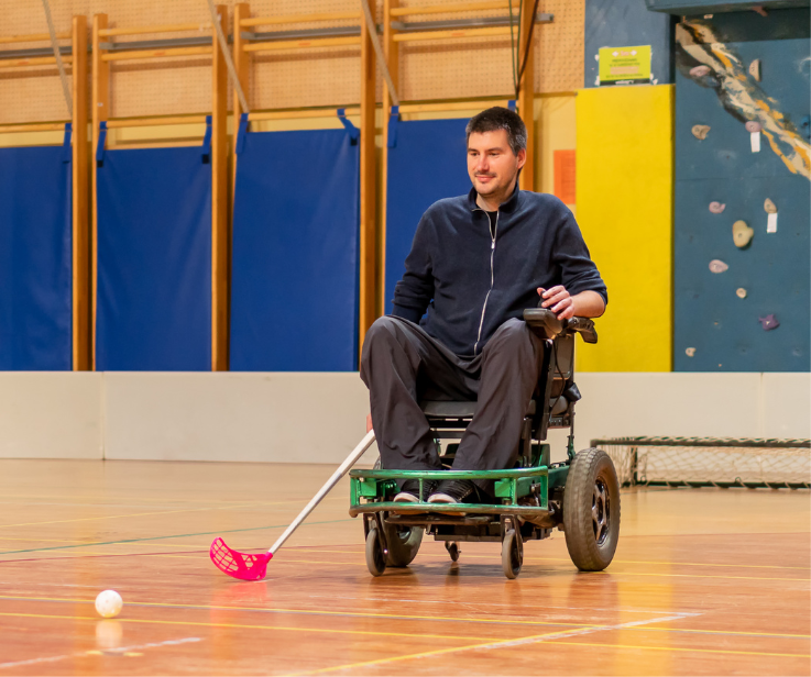 A wheelchair user plays street hockey on a court.