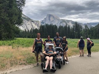 A group of smiling people wearing matching t shirts pose for the camera with Half Dome in the background.