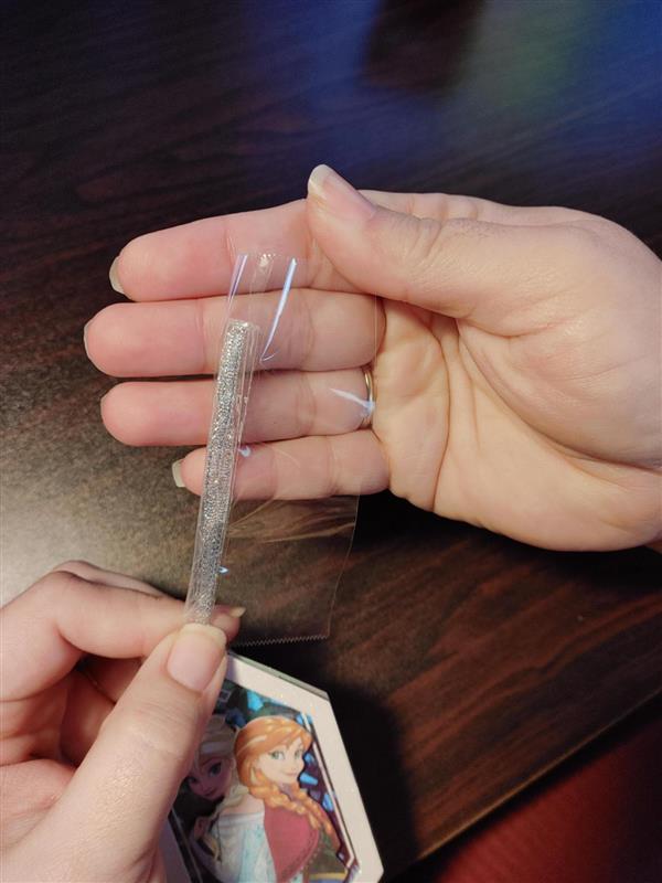 Hands hold a Frozen themed gift tag with the ribbon of the tag being wrapped in clear packing tape
