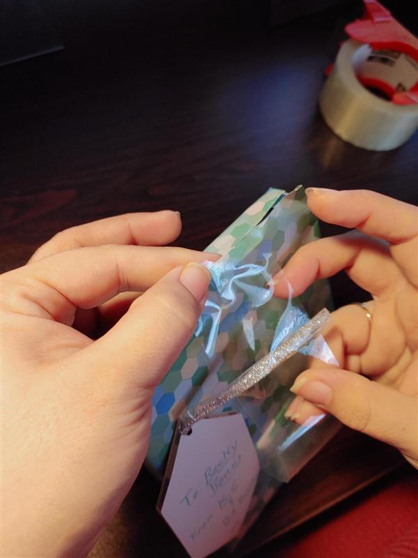 Hands apply the top of the tape strip to the top, untaped seam, of the wrapped gift.