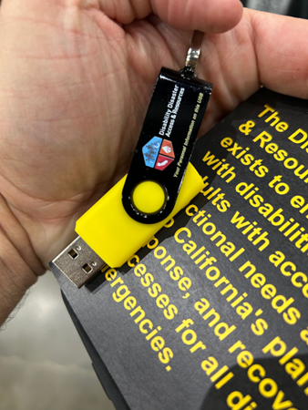 A hand holding a usb stick with the DDAR logo with a flyer in the background.