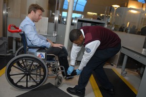 man in wheelchair at airport secutiry and TSA person is wearing blue gloves and checking the man's feet.