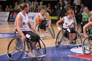 on the basketball court, shows 4 women going for the ball in wheelchairs