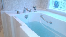 picture of an accessible tub with a walk in door and blue water inside the white tub with silver metal handles