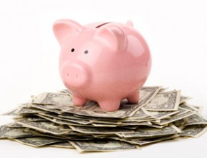 Small pink piggy bank standing on top of a pile of money 
