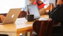 Picture of 2 laptops at a table with a cup of coffee on it and a boy in the background faded out