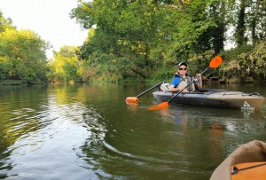 picture of young man padddling in kayak with adaptive paddle in back of kayak