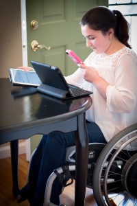 picture of woman using two tablets and smart phone and wheelchair at table