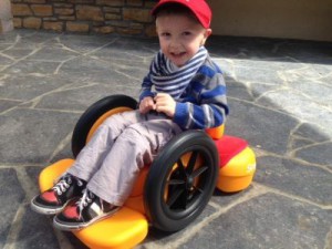 Picture of little boy in red hat sitting on the orange firefly scoot outside