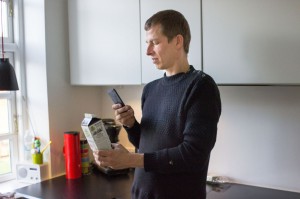 Man standing in kitchen holding his phone up to a milk carton 