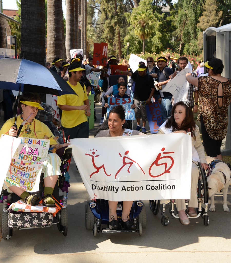 3 women all chair users leading the March at the capitol holding the Disability Action Coalition banner