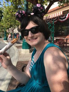 Women sitting on a bench at Disneyland park smiling and eating a churro while wearing dark sunglasses 