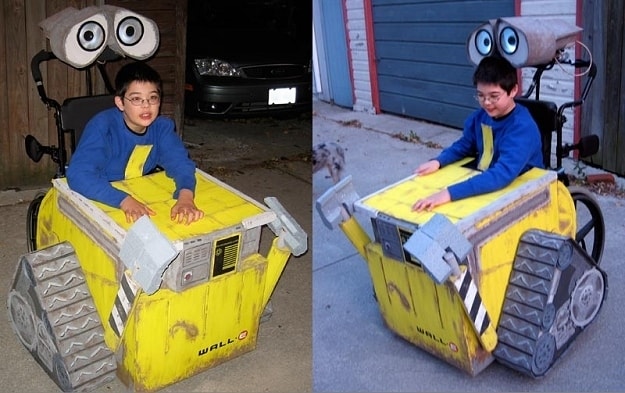 Young boy in his powerchair which is decorated to look like Walle from Disneys pixar film. the little robot is yellow and have large eyes built on the handlebars above the boys head