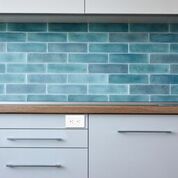There is a cabinet with a bright teal back splash, there is an electrical outlet embedded above the cabinet drawers.