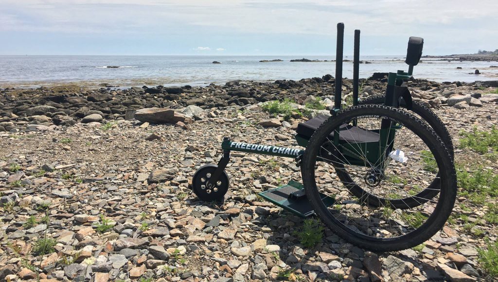 Side view of the green GRIT Freedom Chair sitting on a rocky beach 