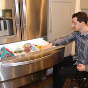 Man sitting in manual chair accessing a lower drawer to an amour style refrigerator 