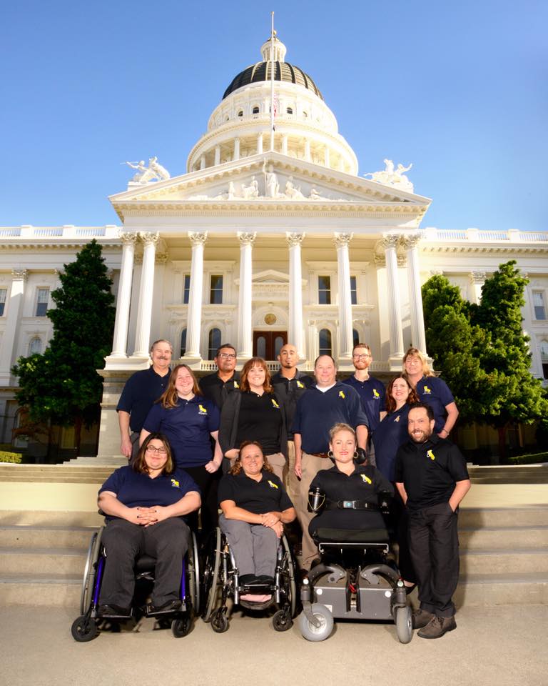 A group of 13 people wearing CFILC shirts are in front of the California Capitol Building.