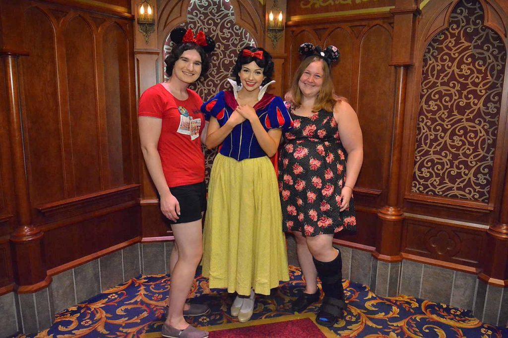 A photo of three women, one is dressed as Snow White and the others are wearing Mouse ears. One of the women is wearing a walking boot.