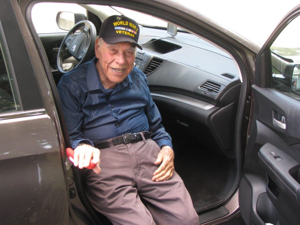 A senior male wearing a Vietnam Veterans hat is using the handy bar to help get out of the car.