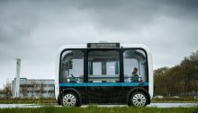 olli bus self drives through a campus with people sitting inside