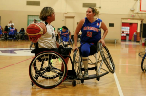 Two women are playing wheelchair basketball. The one on the left has the ball, Alicia is on the right trying to block her.