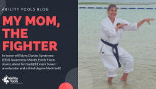The image is of a woman standing in ankle deep water. She is wearing a traditional white karate uniform with her black belt. She is in a karate pose. The text is on a dark blue background. It is white and red, it reads "Ability Tools Blog My Mom, The Fighter. In honor of Ehlers-Danlos Syndrome (EDS) Awareness Month, Emily Flynn shares about her bad@ss mom Susan--an educator and a third degree black belt!"