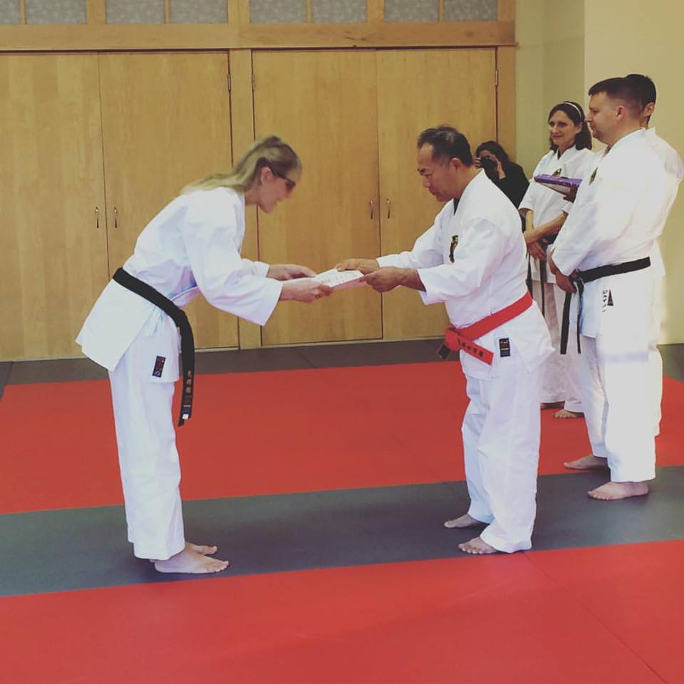 women in traditional martial arts uniform bowing towards man handing her a certificate