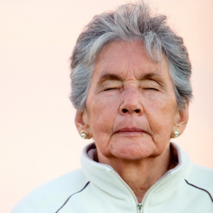 Elder woman in a track jacket with her eyes closed.