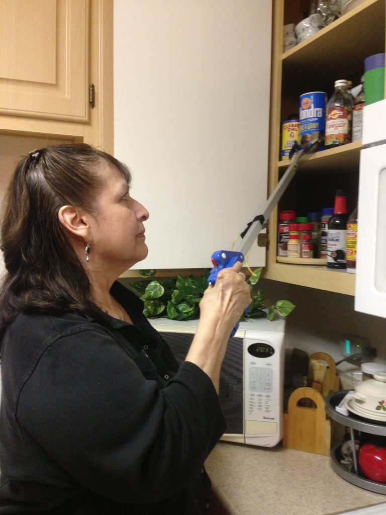 Woman using reacher/grabber tool to get item in kitchen cupboard.